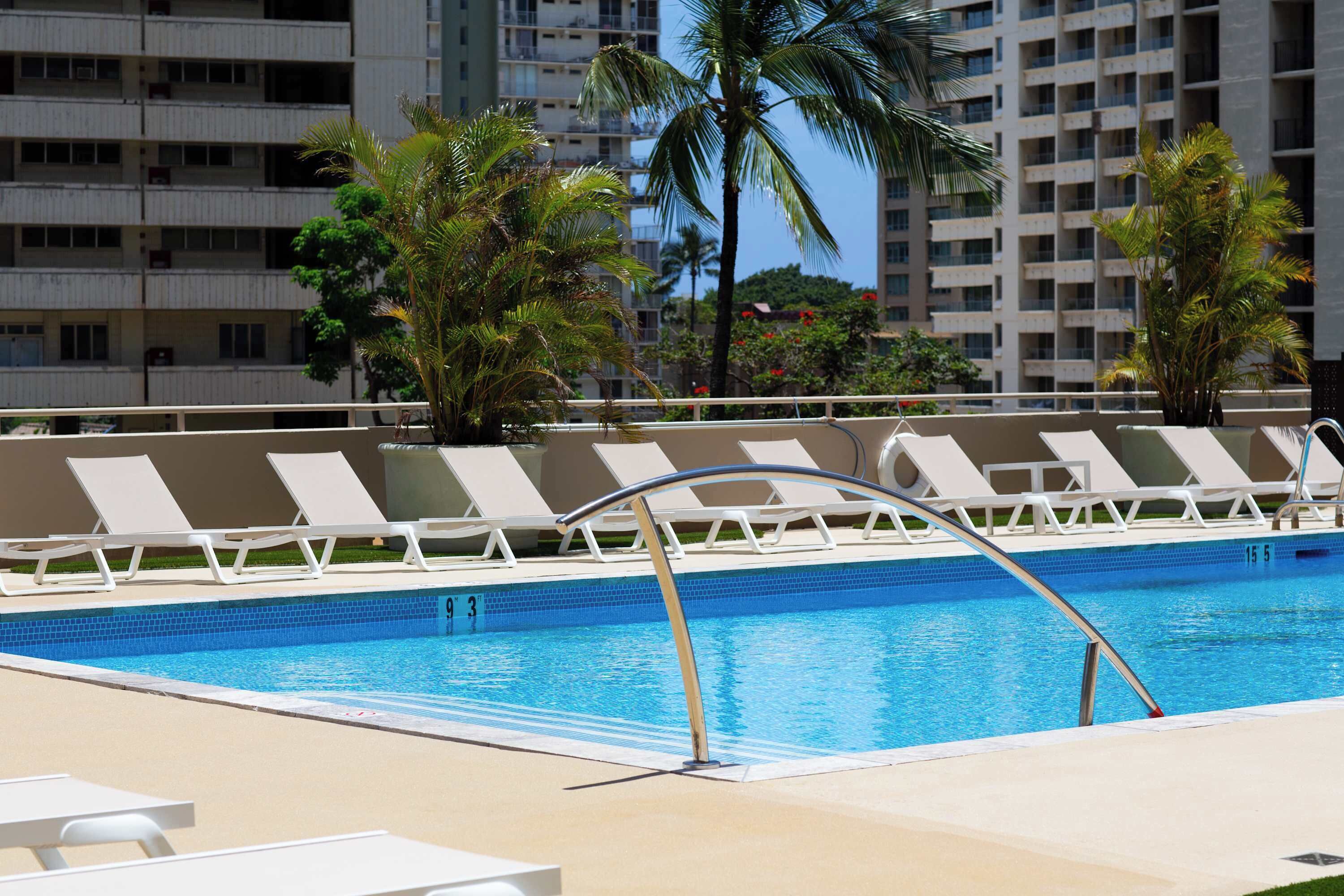 A swimming pool with lounge chairs and palm trees.