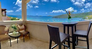 A balcony with wicker chairs and a small table, overlooking a turquoise sea with boats and a hilly landscape. - Aahana Two Bedroom (Cruz Bay, St. John)