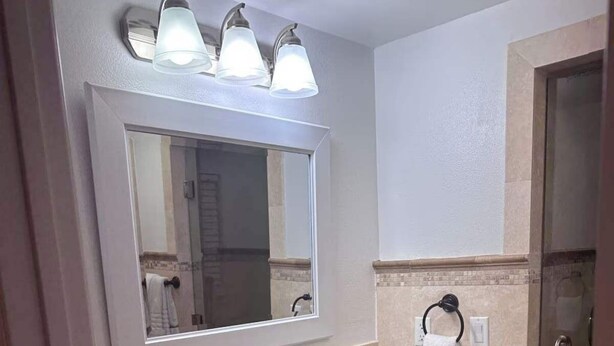 Een badkamer met een wastafelblad van graniet, witte badkasten, een grote spiegel en een douchecabine van glas.