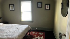 Un dormitorio con una cama, un ventanal y tres cuadros en la pared.