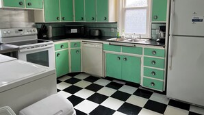 Una cocina con armarios verdes, piso a cuadros blanco y negro, estufa, lavavajillas y refrigerador.