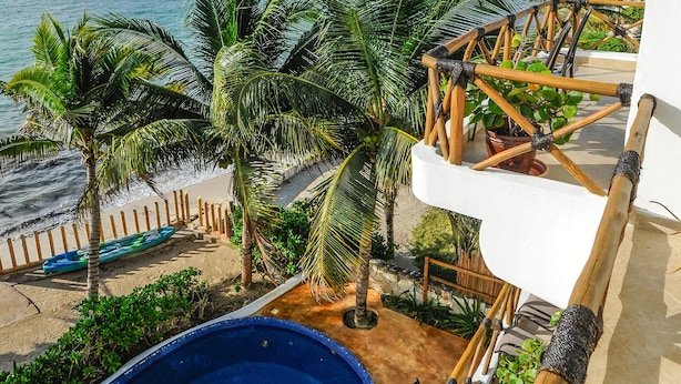 A pool with a view of the beach and ocean, surrounded by palm trees and a thatched roof structure.