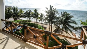 A balcony with a view of the beach, palm trees, and a distant building.