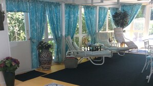 A sunlit room with a large window, blue curtains, a patterned rug, and two lounge chairs. - Alnwick Cottage, quaint and comfortable (Niagara on the Lake)