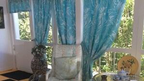 A room with a single bed, a small table with a teapot and cups, a potted plant, and a window with blue curtains. - Alnwick Cottage, quaint and comfortable (Niagara on the Lake)