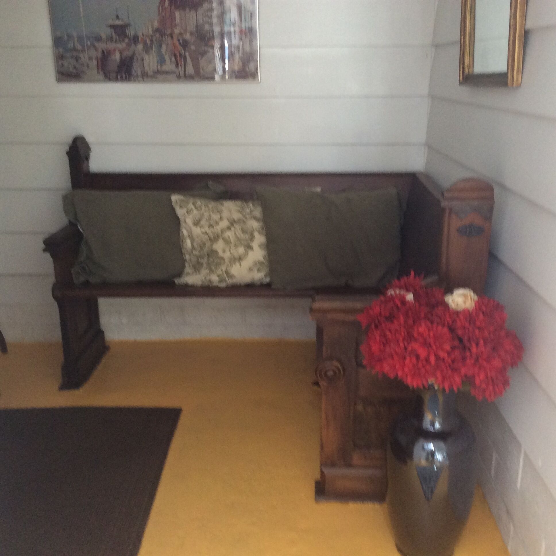 A room with a wooden bench, a vase with red flowers, and a framed picture on the wall.