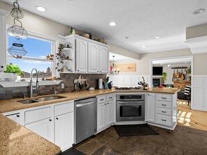 Eine moderne Küche mit weißen Schränken, Granit Arbeitsplatten, einer Spülmaschine, einem Backofen und einem Gasherd.
