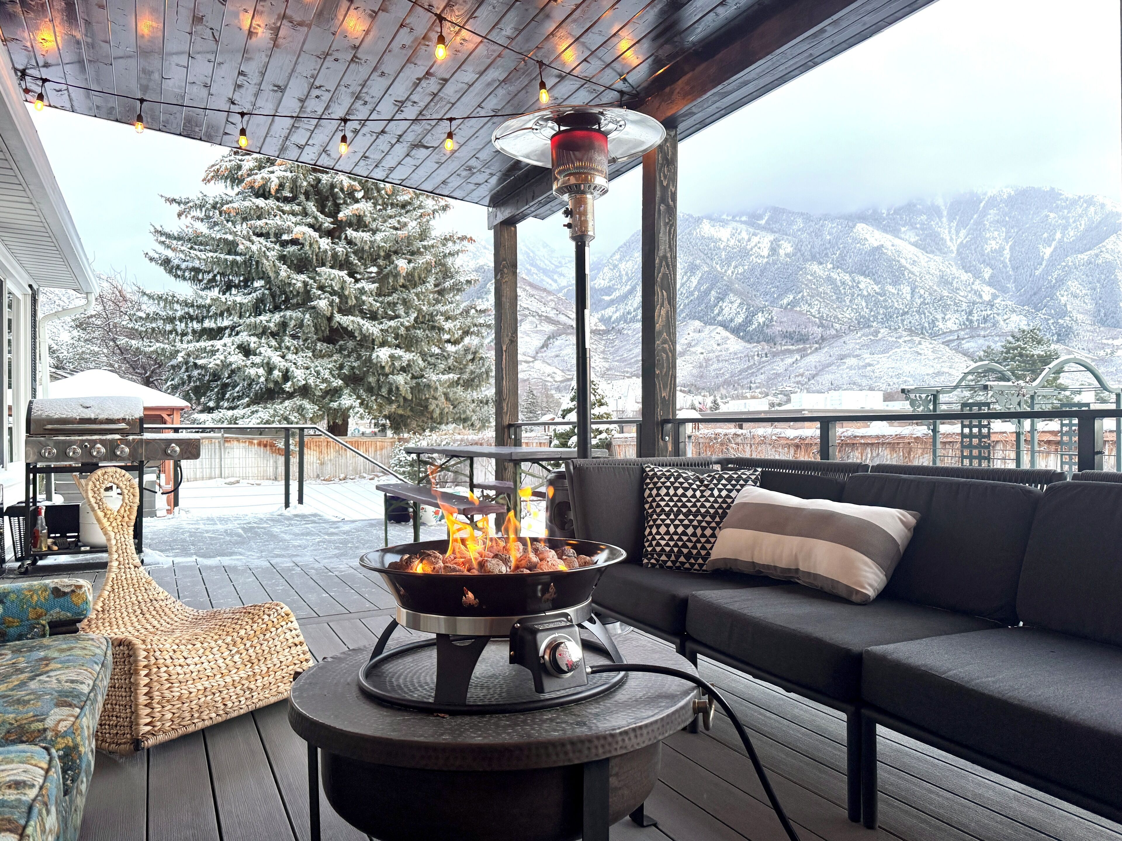 A cozy outdoor seating area with a wood-burning stove, a sofa, and a view of snow-covered mountains.