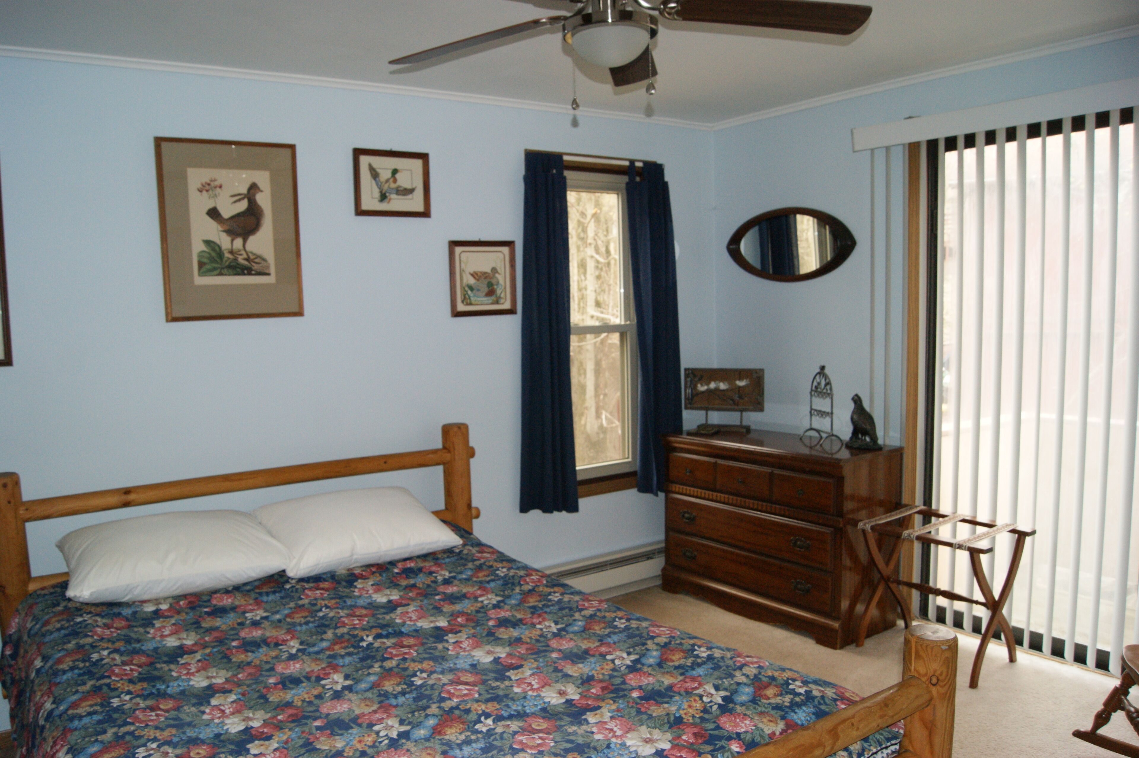 A bedroom with a wooden bed, a dresser, a mirror, and a ceiling fan.