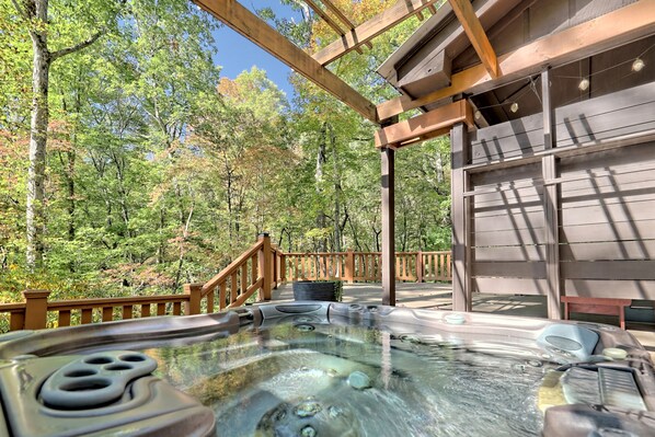 A hot tub with a wooden deck and a view of a forest.