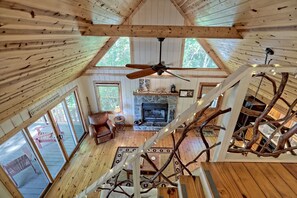 A cabin interior with a fireplace, wooden floors, and a ceiling fan.