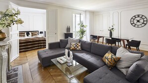 Un salon moderne avec un canapé gris, une table basse en verre et un coin repas comprenant une table et des chaises.