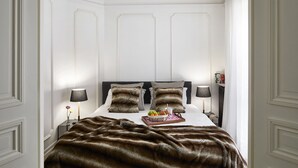 Une chambre à coucher avec un grand lit, deux tables de chevet, une lampe de chaque côté, et un plateau avec des fruits et une boisson sur le lit.