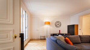 Un salon avec un canapé, une lampe, une horloge et un téléviseur.