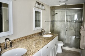 Une salle de bain avec deux lavabos, un miroir et une douche à parois de verre.