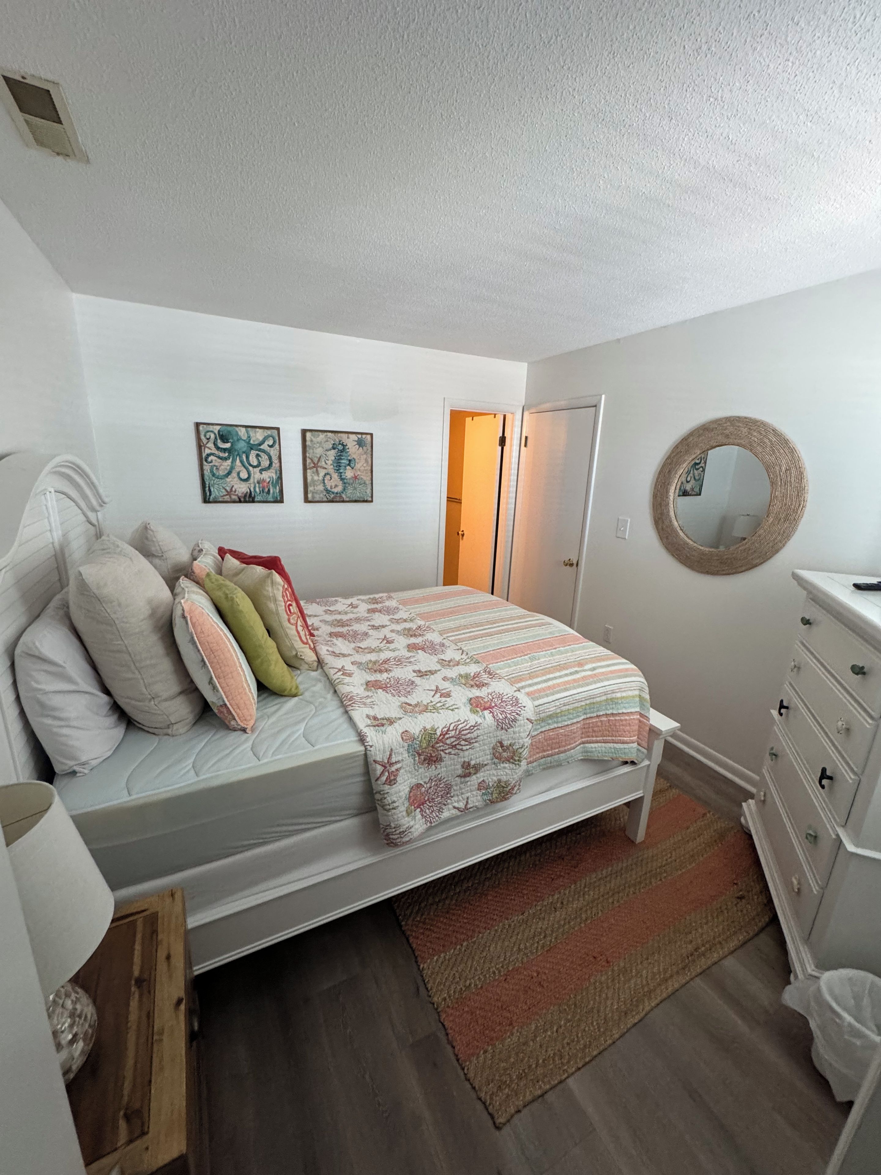 Una camera da letto con un letto, una cassettiera, uno specchio e due elementi decorativi a parete.