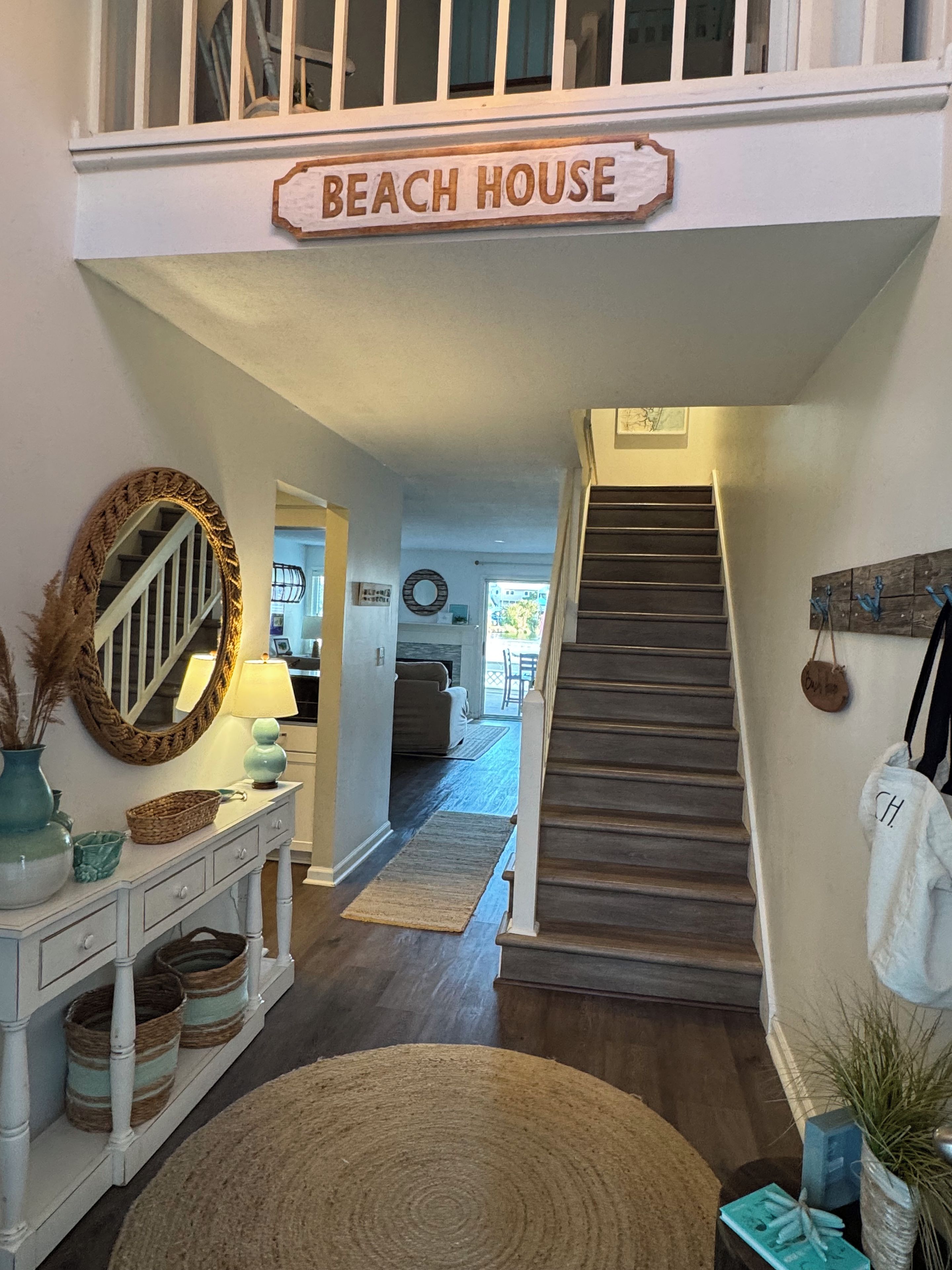 Een trap die leidt naar een tweede verdieping, met daar boven een bordje dat 'BEACH HOUSE' vermeldt.