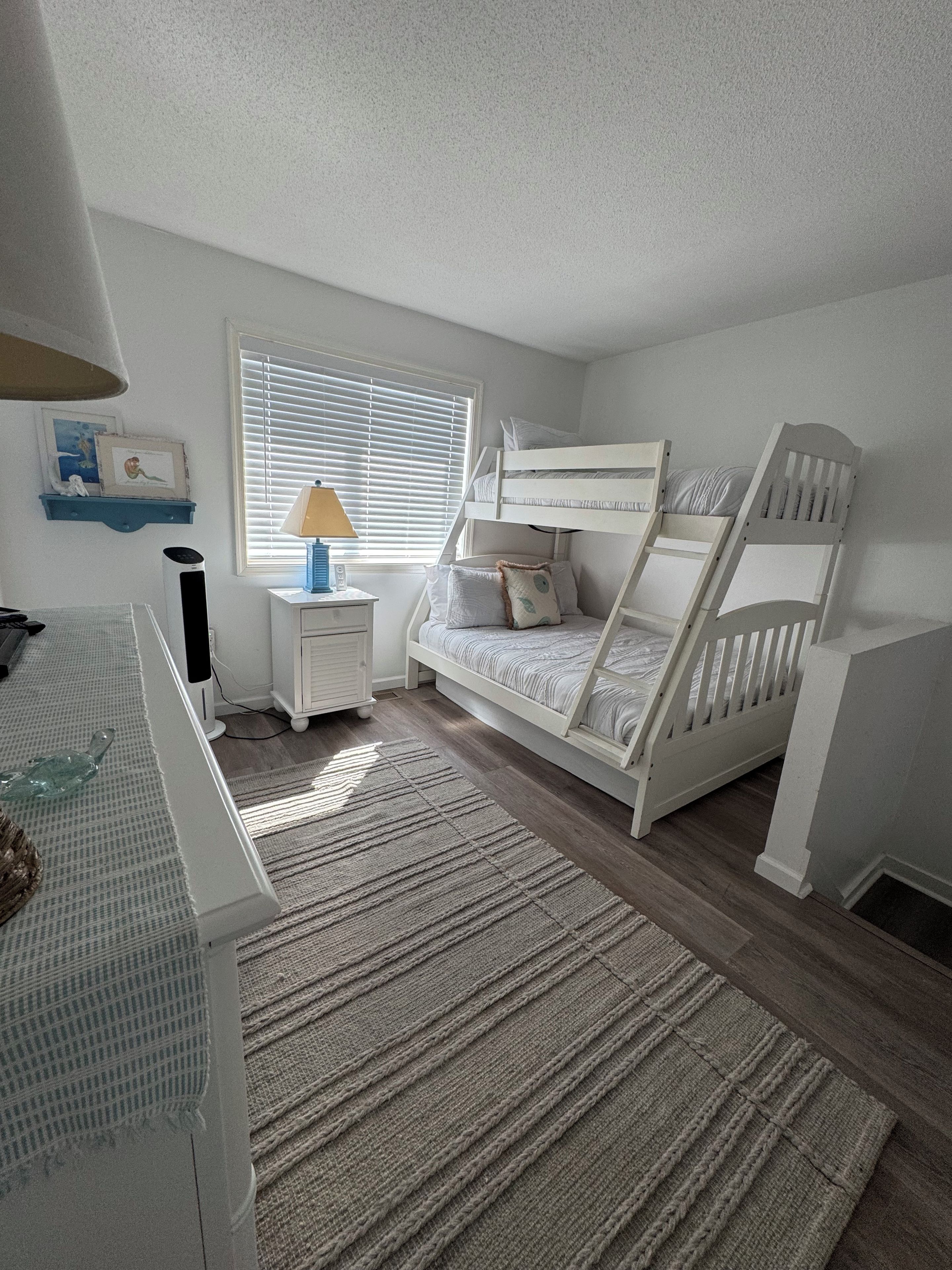 A child's bedroom with bunk beds, a desk, a lamp, and a window with blinds.