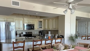 A spacious kitchen with a central island, wooden chairs, and a ceiling fan. - Oceanfront Condo - Fantastic Views, Beautiful Furnishings!  (Folly Beach)