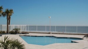A swimming pool with a white fence and palm trees in the foreground. - Oceanfront Condo - Fantastic Views, Beautiful Furnishings!  (Folly Beach)