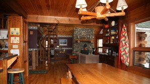 L’intérieur d’un chalet rustique, avec une table à manger en bois, une cheminée en pierre et un coin salon confortable.
