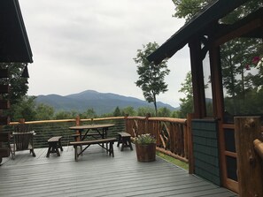 Um deck de madeira com mesas de piquenique e vista para montanhas.