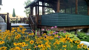 Une terrasse en bois dotée d’un espace salon abrité, entourée de fleurs aux couleurs vives, jaune et violet.