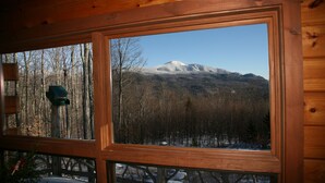Une cabane dotée d’une grande fenêtre donnant sur une montagne enneigée et une zone boisée.