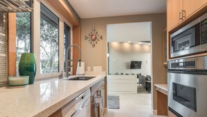 A modern kitchen with stainless steel appliances, a large window, and a view of the outdoors. - Renovated Mid-Century Mod Home with Spectacular Views in Point Loma (Spa & A/C) (San Diego)