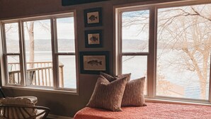 Ein Schlafzimmer mit einem großen Bett, Holzboden, einem Schaukelstuhl und Seeblick durch große Fenster.
