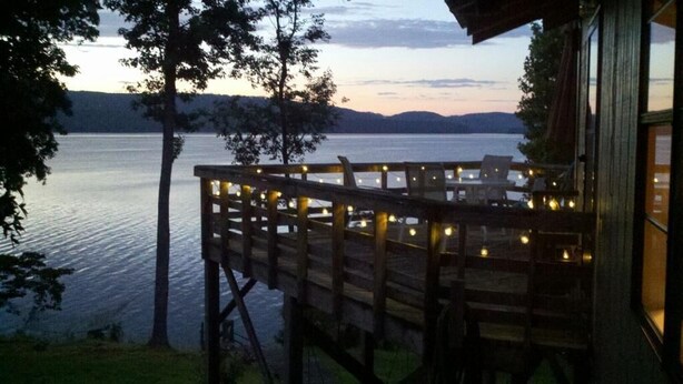 Eine Holzterrasse mit Lichterketten, die auf einen See im Dämmerlicht blickt.