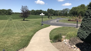 A paved pathway leading to a roundabout with a fountain and a bird statue. - PICKLEBALL, Heated Pool, Game Room, Outdoor Oasis, Tennis, Basketball, & woods! (Griggsville)