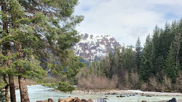 Ein Campingplatz mit Adirondack-Stühlen, einer Feuerstelle und Blick auf einen Fluss.