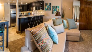 A modern living room with a beige sofa, a dining area with a table and chairs, a kitchen with dark cabinets and a stainless steel refrigerator, and a large window with curtains. - 500 Ft. From Slope! Remodeled Studio  (Steamboat Springs)