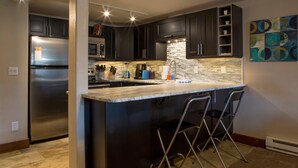 A modern kitchen with dark cabinets, a stainless steel refrigerator, a built-in oven, and a granite countertop. - 500 Ft. From Slope! Remodeled Studio  (Steamboat Springs)
