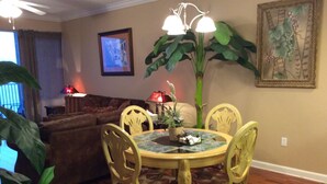 A dining area with a round table, four chairs, a potted plant, and a painting on the wall.
