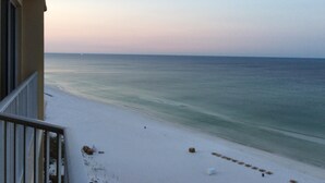 A balcony with a view of a beach and ocean during sunset.