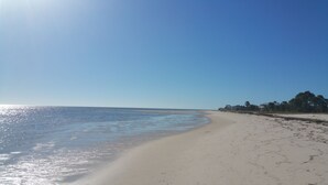 Ein weiter Sandstrand mit sanften Wellen, blauem Himmel und ein paar Gebäuden in der Ferne.
