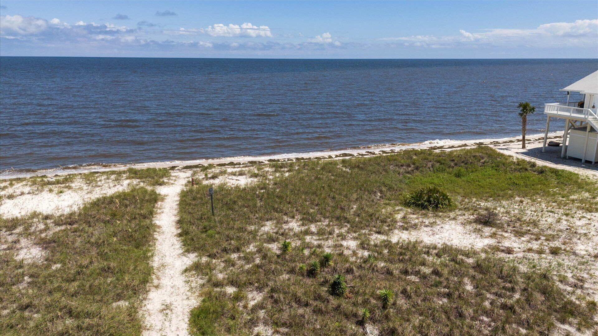 Une vue sur la côte, avec une plage de sable, un bâtiment blanc doté d’un balcon et une vue dégagée sur l’océan.