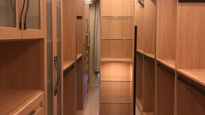Un vestidor con estantes y cajones de madera, con una puerta espejada y luces en el techo.