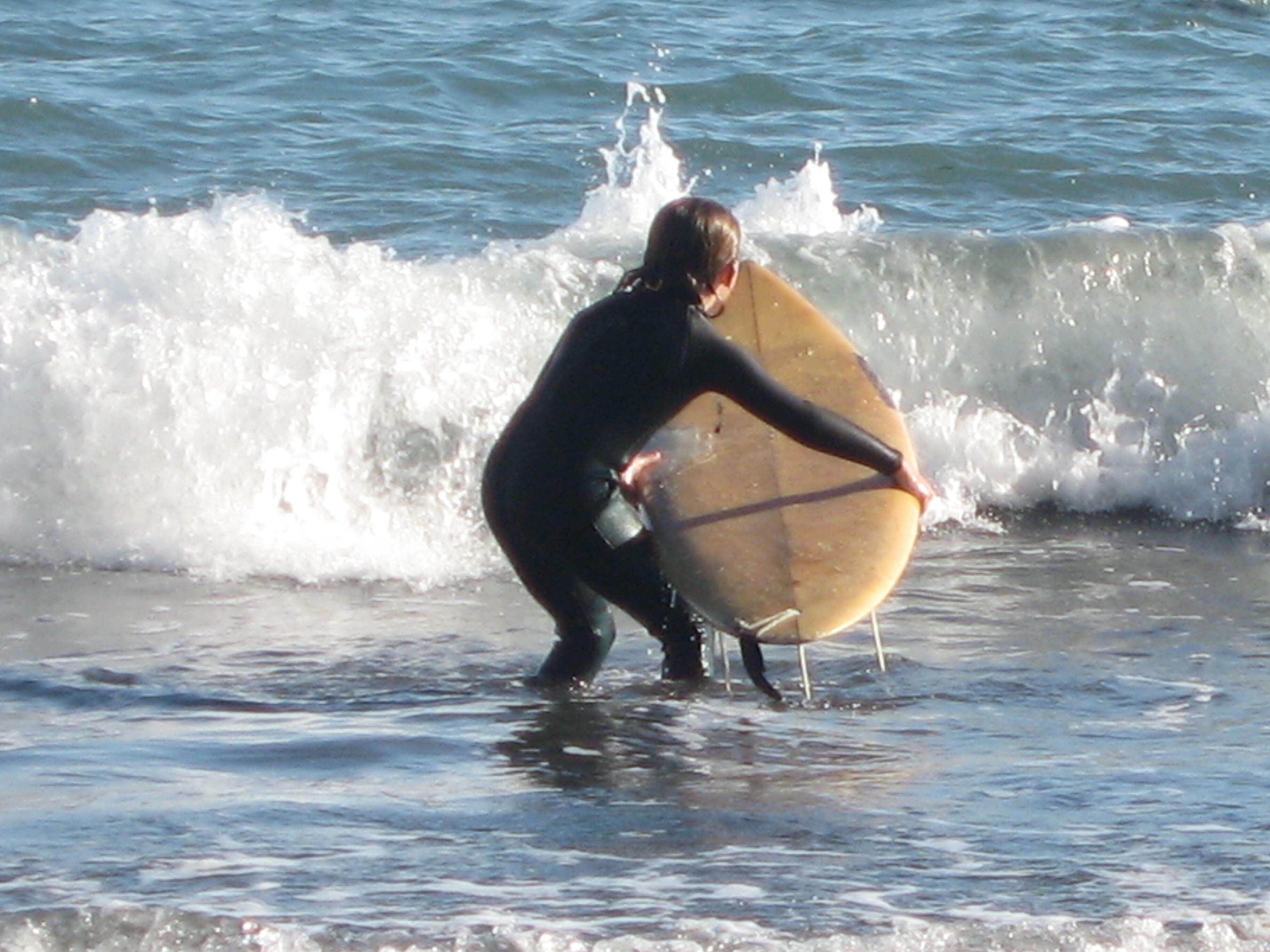 Iemand in een neopreenpak die een surfplank vasthoudt aan het strand.