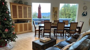 Una sala de estar acogedora con un sofá de cuero, una zona de comedor con sillas de madera, un árbol de Navidad y vistas al exterior.