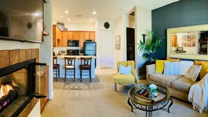 A living room with a fireplace, a dining area with chairs, a sofa with cushions, and a coffee table with decorative items.