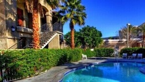 A swimming pool with lounge chairs, palm trees, and a building with a staircase.