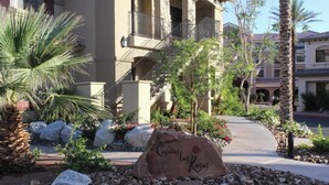 A building with a stone sign reading "Casitas Las Palmas" surrounded by rocks, palm trees, and a pathway leading to the entrance.