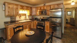 Cucina con mobili in legno, elettrodomestici in acciaio inossidabile, forno a microonde, forno e frigorifero. C'è un tavolo da pranzo con sedie e un cesto sul bancone.