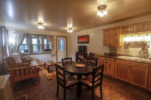 Una sala de estar acogedora con un sofá, una mesa de comedor con sillas, una cocina con armarios de madera y una ventana con cortinas.