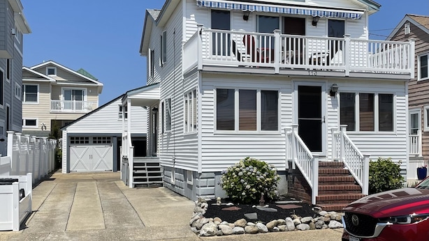 A two-story house with a front porch, a garage, and a small garden area with rocks and plants.