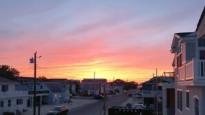 A residential street at sunset with houses and parked cars.