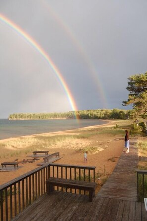 A wooden deck overlooking a beach with a rainbow in the sky.
